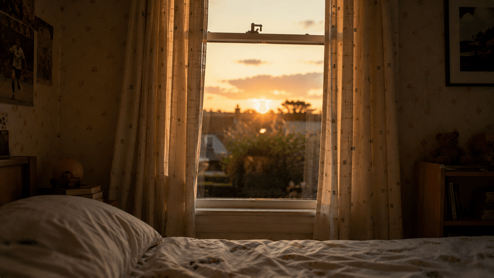 Child’s bedroom at dusk seen from bed level, looking toward an open window with curtains parted and warm evening light beyond.